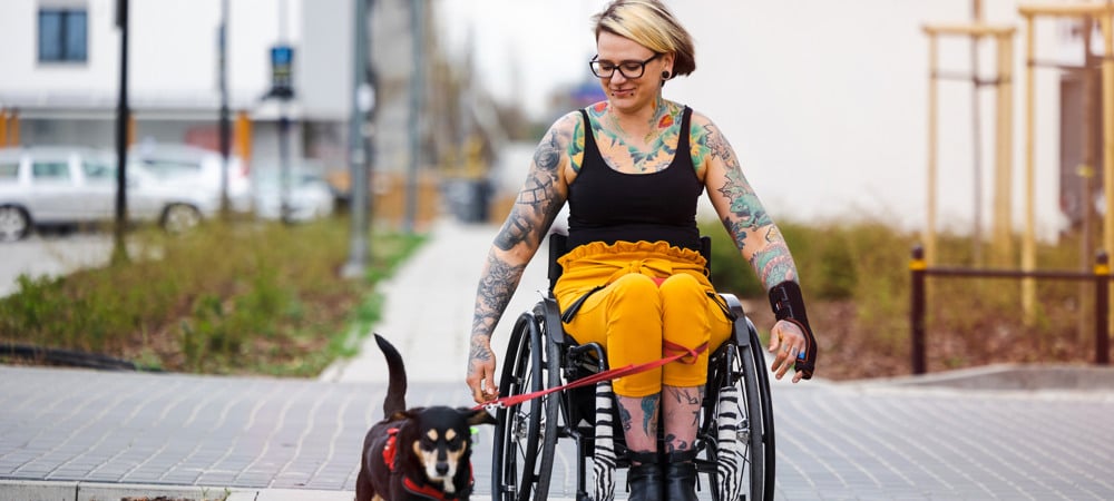 En kvinna i rullstol med en hund i koppel.