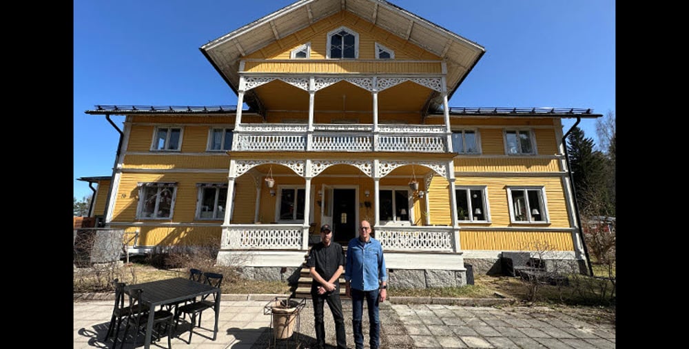 Två personer utanför stort gult hus