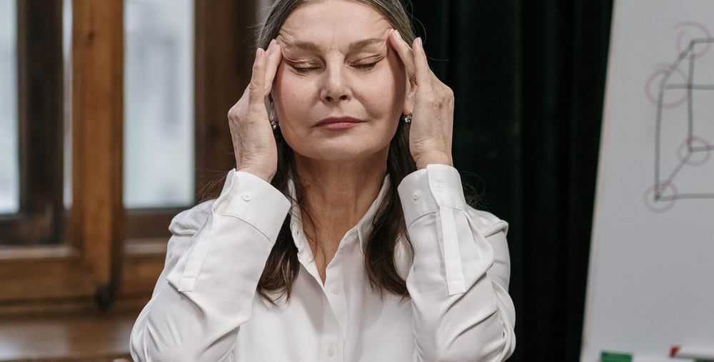 Person som sitter vid konferensbord, blundar och masserar tinningarna.