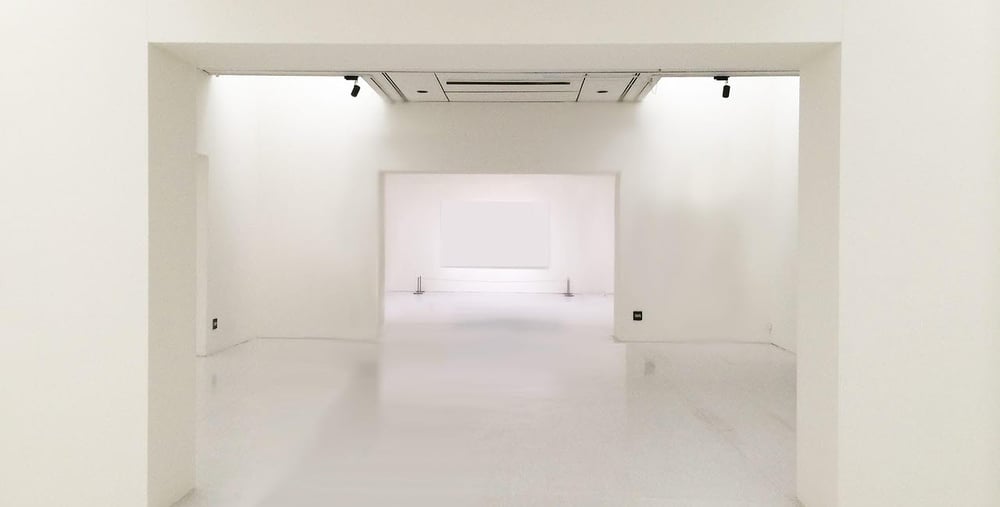 Tomt utställningsrum med vita väggar, tak och golv i flera öppna sektioner.