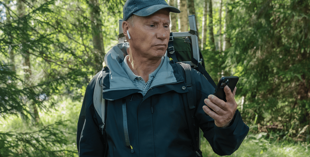 En man som står i skogen och tittar på sin mobiltelefon.