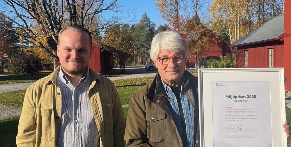 Två män står bredvid varandra i utomhusmiljö på hösten. Den ena håller i ett inramat diplom för Miljöpriset 2025.