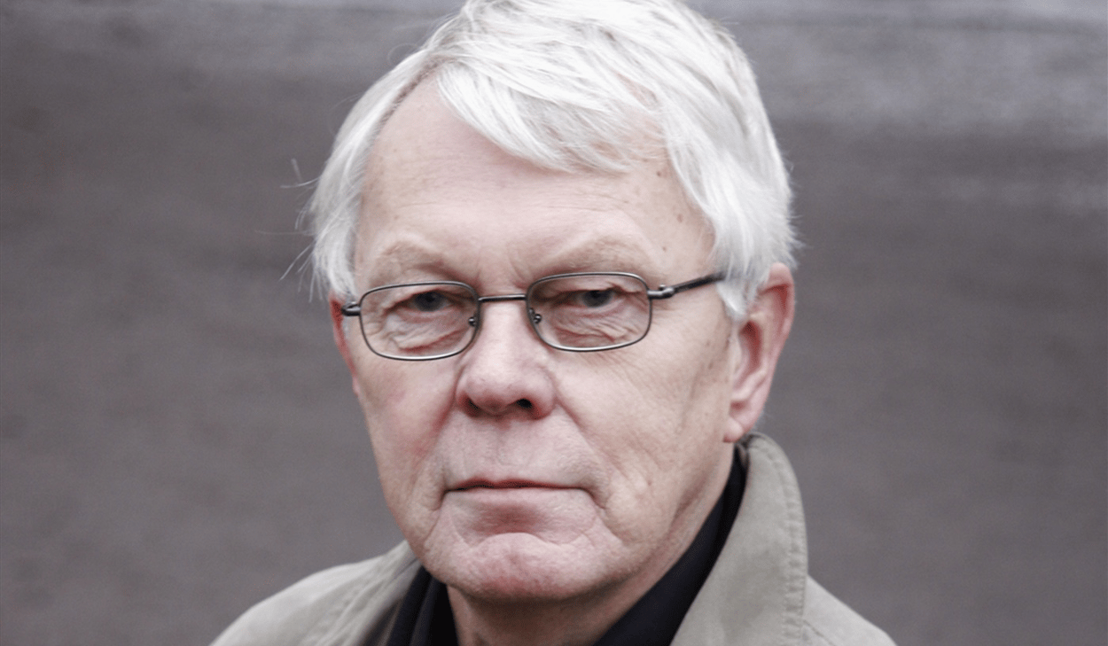 En man med vitt hår som bär en trenchcoat.
