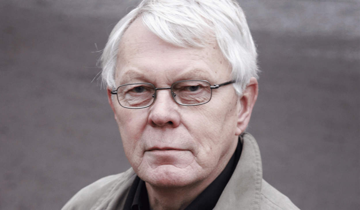 En man med vitt hår som bär en trenchcoat.