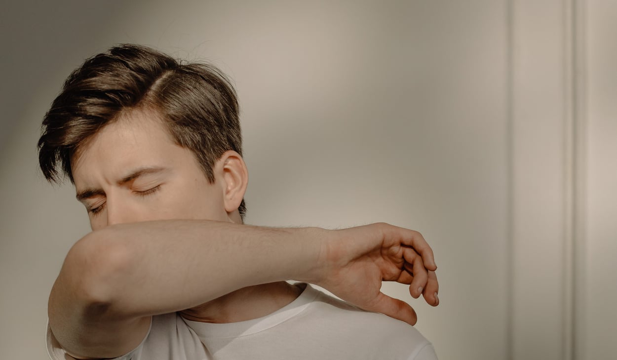 Person som verkar vara förkyld och nyser i armvecket.