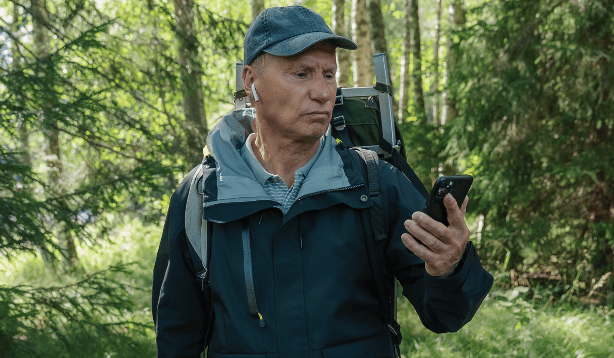 En man som står i skogen och tittar på sin mobiltelefon.