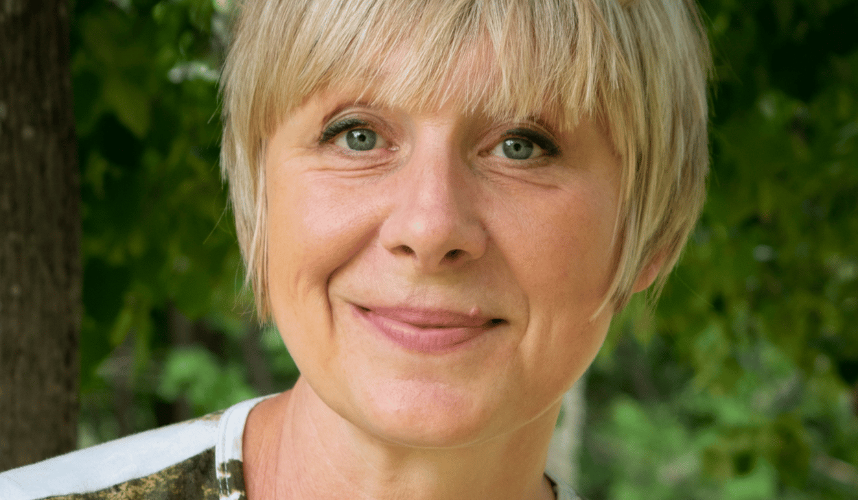 En kvinna med blont hår ler mot kameran.