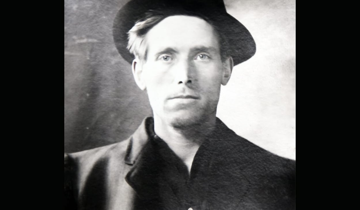 Svartvit bild av författare Joe Hill iklädd rock och hatt. 
