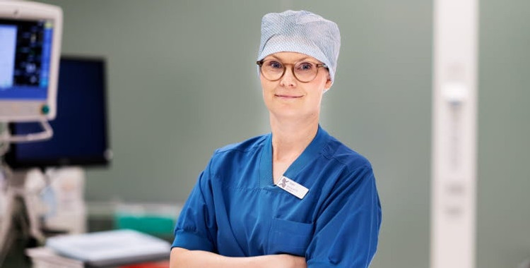 En kvinna i operationskläder och glasögon som står på ett sjukhus.