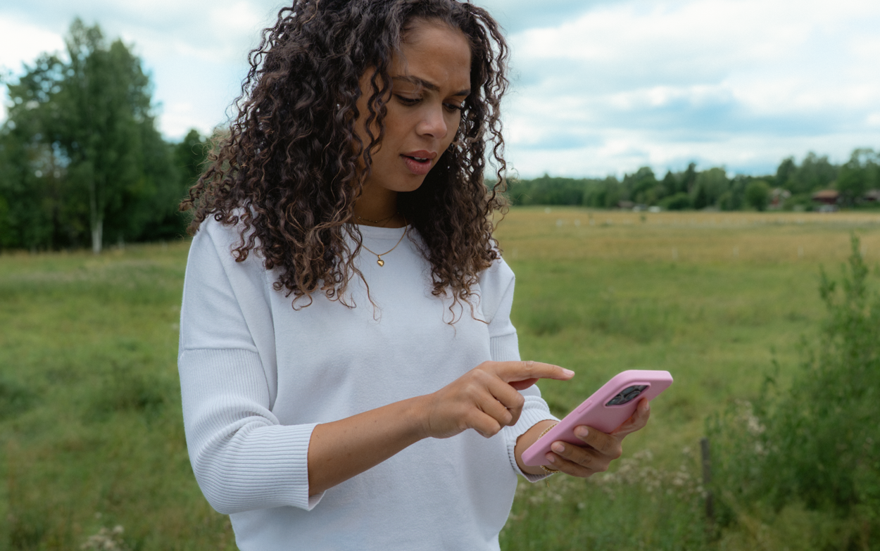Kvinna st&aring;r utomhus och anv&auml;nder en mobiltelefon.
