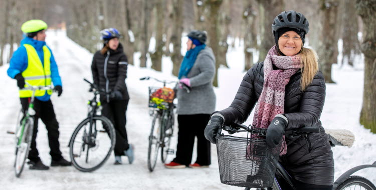 Personer står med sina cyklar på snötäckt cykelbana. 