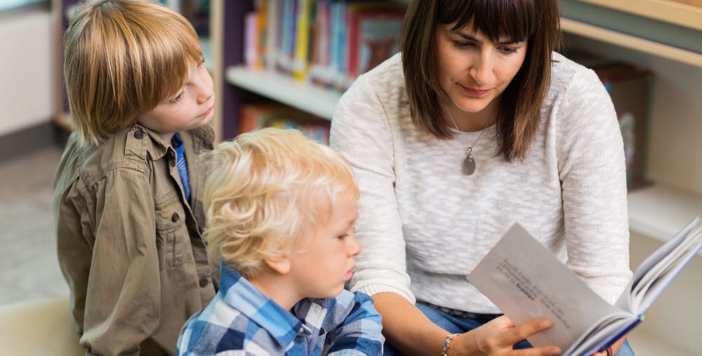 Young teacher reading book for students in school library