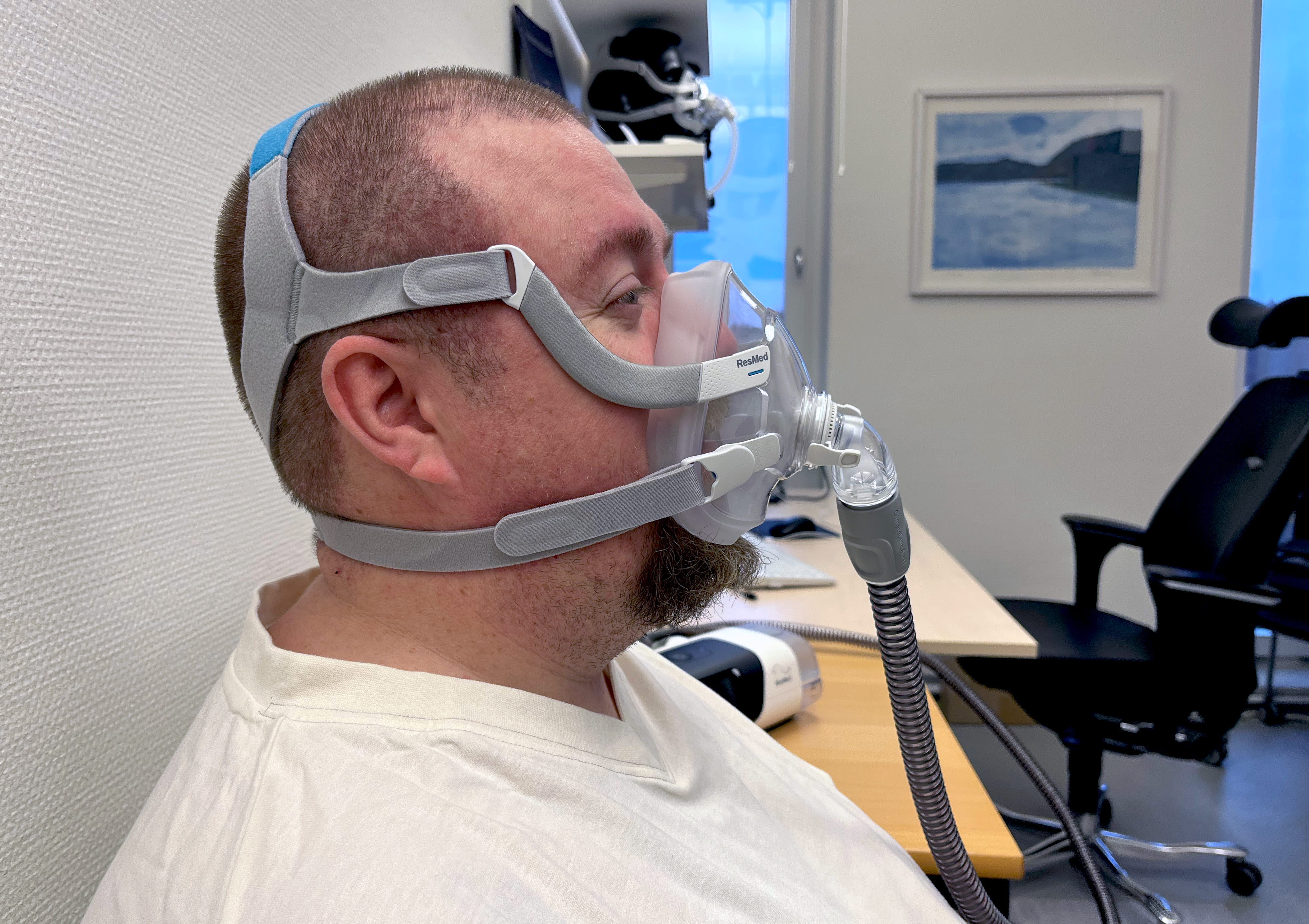 En man - en patient - sitter med en ansiktsmask över näsa och mun. Profilbild. 