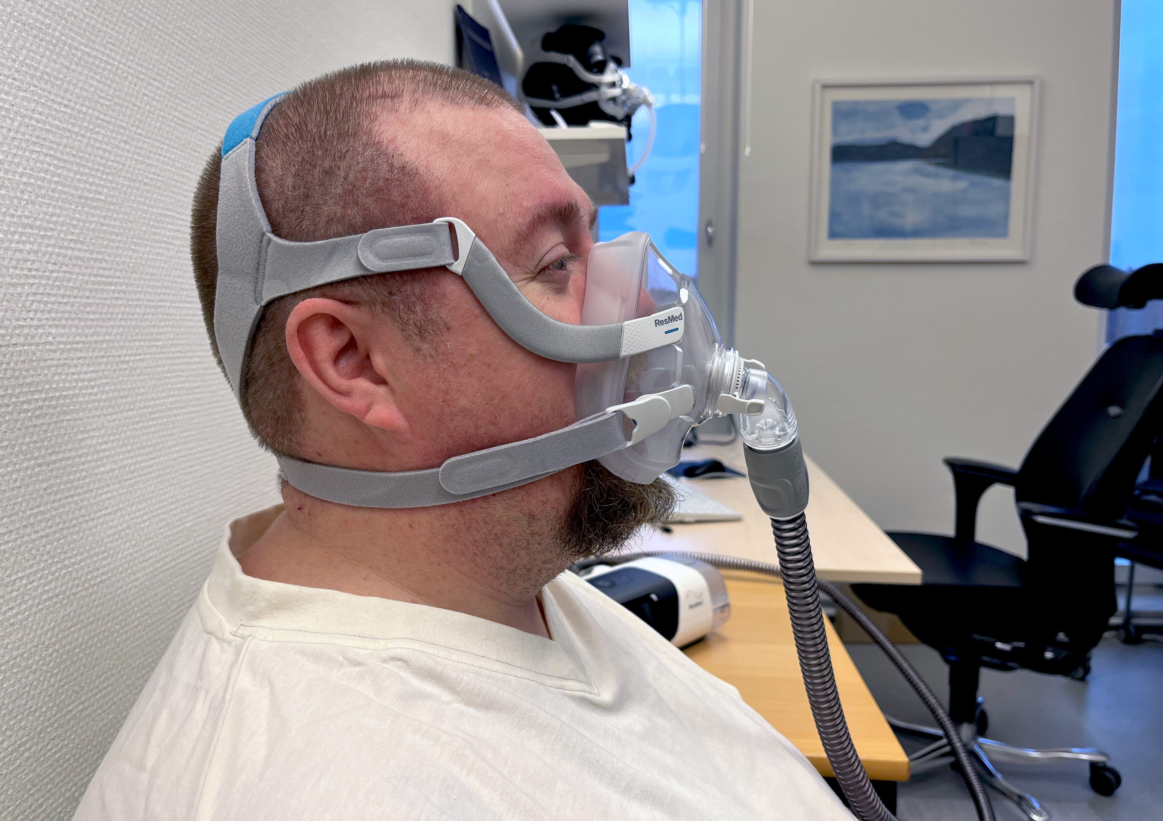 En man - en patient - sitter med en ansiktsmask över näsa och mun. Profilbild.