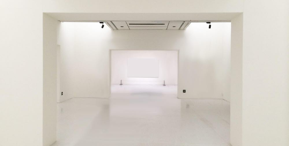 Tomt utställningsrum med vita väggar, tak och golv i flera öppna sektioner.
