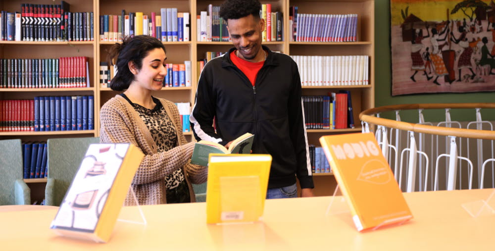Två kursdeltagare står i ett bibliotek och tittar ned i en bok