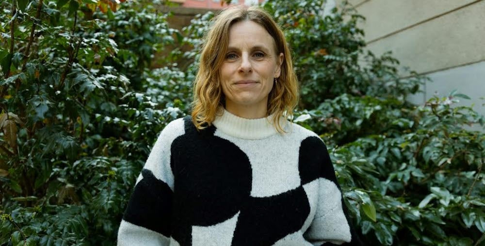 Person ståendes framför en grön buske iklädd en svart och vit mönstrad tröja.