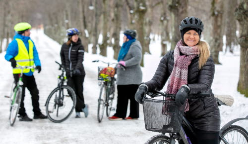 Personer står med sina cyklar på snötäckt cykelbana. 