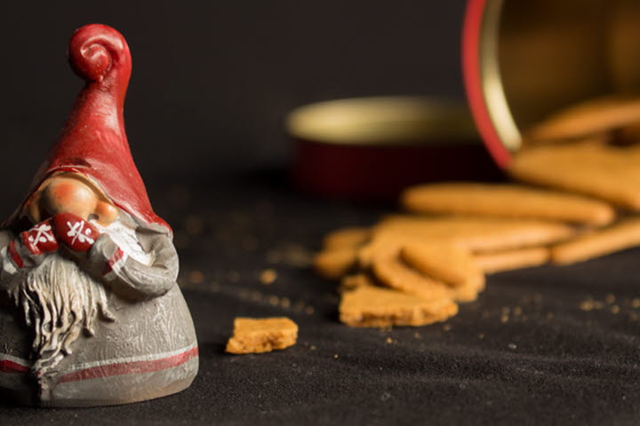Porslinstomte på bord framför pepparkakor i en hög