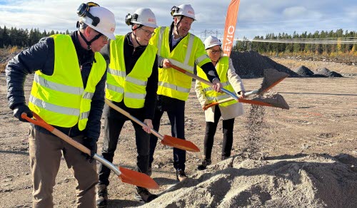 Fyra personer i bygghjälmar och reflexvästar tar första spadtaget med varsin spade på en byggarbetsplats.