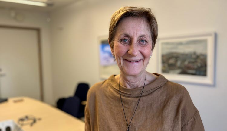 Kvinna med kort hår, brun långärmad tröja, ser in i kameran med litet leende.