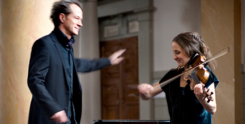 Lisa Rydberg och Gunnar Idenstam står framför ett piano och spelar fiol.